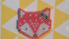 a red and white beaded fox brooch sitting on top of a yellow and white checkered tablecloth