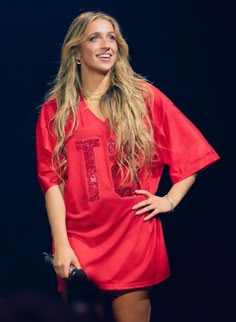 a woman in a red dress standing on stage with her hands on her hips and smiling at the camera