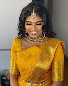 a woman wearing a yellow sari with gold jewelry on her neck and shoulders, smiling