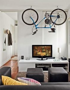 a bike hanging from the ceiling above a desk with chairs and a television on it