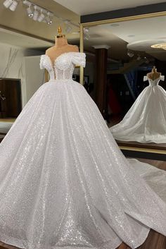 a white wedding dress with sequins on the skirt and off the shoulder, in front of a mirror