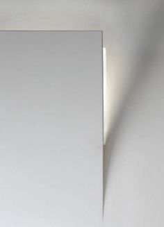 a white wall with a light on it and a mirror in the corner next to it