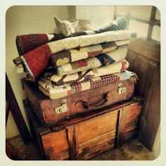 a pile of luggage sitting on top of a wooden dresser next to a window with a cat laying on top of it