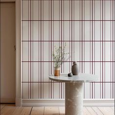 a table with two vases on it in front of a wallpapered room