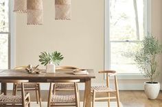 a dining room table with four chairs and a potted plant in the center, next to two windows