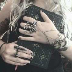 a woman holding a book with rings on her fingers and an inverted pentagramil ring