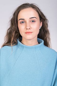 a woman with long hair wearing a blue sweater and earring, looking at the camera