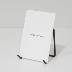 a white sign sitting on top of a table next to a black metal stand with the words shop copack written on it