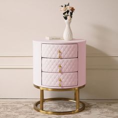 a white vase with flowers on top of a pink and gold dresser next to a wall