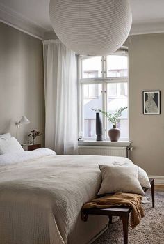 a bedroom with a large bed and white curtains on the window sill above it