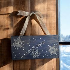 a wooden sign that says let it snow hanging on the side of a building next to a window