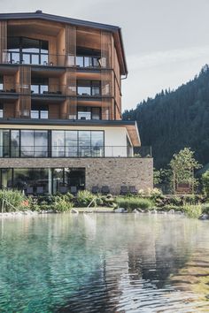 a large building next to a body of water with trees and mountains in the background