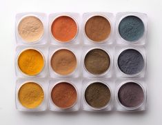 six different colored powders in a plastic container on a white surface with the lids open