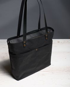 a black tote bag sitting on top of a wooden table next to a bottle