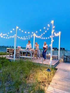 three people sitting on a dock with lights strung over them