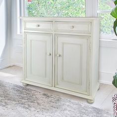 a white cabinet sitting in front of a window next to a potted green plant