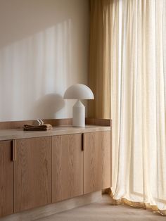 two lamps on top of a wooden cabinet in front of a window with drapes