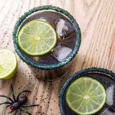 two glasses filled with black magic margaritas on top of a wooden table next to a spider