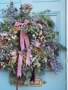 a wreath with pink ribbon hanging on a blue door decorated with greenery and flowers