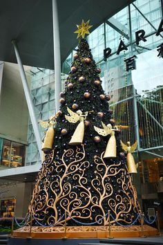 a large christmas tree in the middle of a shopping mall with gold bells and angel decorations on it