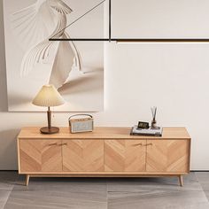 a wooden sideboard with a lamp and pictures on the wall behind it in an empty room