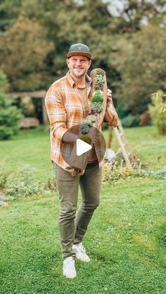 a man standing on top of a lush green field holding a plant in his hand