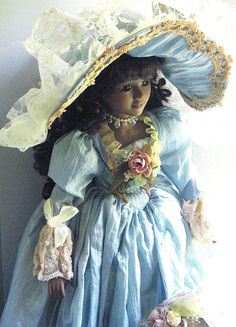 a doll wearing a blue dress and large hat with flowers on it's head