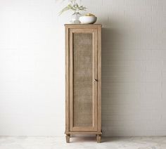 a tall wooden cabinet sitting in front of a white wall with a vase on top