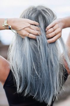 a woman with long grey hair is holding her hands on her head and wearing gold bracelets