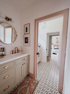 a bathroom with white and pink walls, tile flooring and gold accents on the mirror