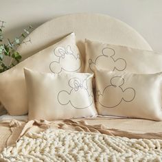 three pillows with mickey mouse drawn on them sitting on a bed next to a plant