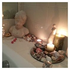 candles and seashells sit on a bathroom counter next to a bathtub with a statue in the background