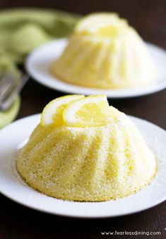 two white plates topped with cakes covered in frosting and lemons next to a fork