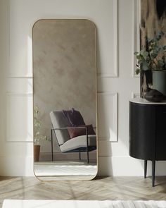 a mirror sitting on top of a wooden floor next to a chair and potted plant