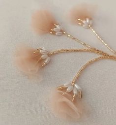 three hair pins with flowers on them sitting on a white tablecloth, one is gold and the other is pink