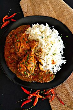 a black plate topped with rice and meat covered in gravy next to red peppers