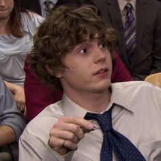 a young man wearing a white shirt and blue tie with people in the background looking at him