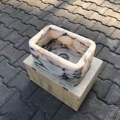 a marble sink sitting on top of a block of wood next to a brick sidewalk