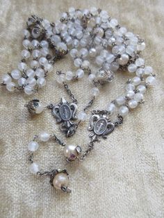 Older vintage rosary parts for jewelry making or repair. These two sections of rosary beads are crafted with glass beads and beautiful sterling silver Fleur Di Lis Blessed Mother Center medals.  I think the beads had a pearl coating that has mostly rubbed off. I think they are lovely as they are. The religious medals are stamped sterling but I don't know if their connecting links are sterling.  They are sold as is as you see here for your project or jewelry making. Their sterling Fleur Di Lis me Handmade Silver Wedding Rosary, Vintage Silver Rosary With Round Beads, Vintage Silver Handmade Rosary, Handmade Vintage Silver Rosary, Handmade Silver Vintage Rosary, Vintage Rosary, Beaded Rosary, Hand Painted Roses, Carved Shell