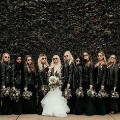 a group of women standing next to each other in front of a wall with plants