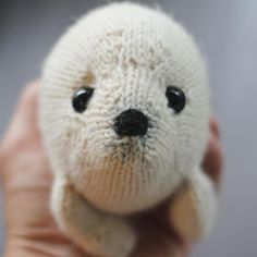 a hand holding a small white stuffed animal with black eyes and nose, in front of a gray background