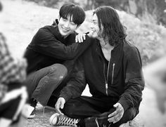 two young men sitting next to each other on the ground with their arms around one another