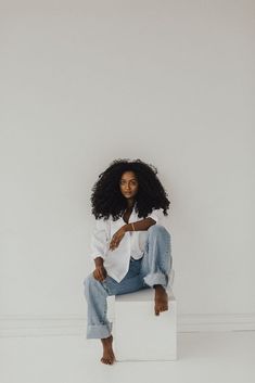 a woman sitting on top of a white block wearing jeans and a white button up shirt