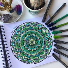 a coloring book surrounded by crayons and pens on a table next to a cactus