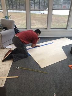 two men working on an area rug in a living room with large windows and flooring