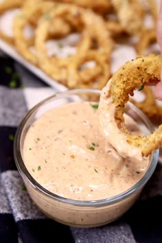 a person dipping something into a small glass bowl with pretzels in the background