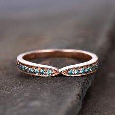 a rose gold wedding band with blue topazte stones on the side, sitting on a rock