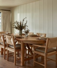 a dining room table and chairs in front of a window with white paneled walls