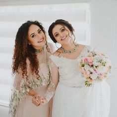 two women standing next to each other in front of a window holding hands and smiling