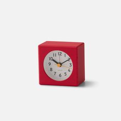 a small red clock with black hands on a white background, it appears to be in the shape of a cube